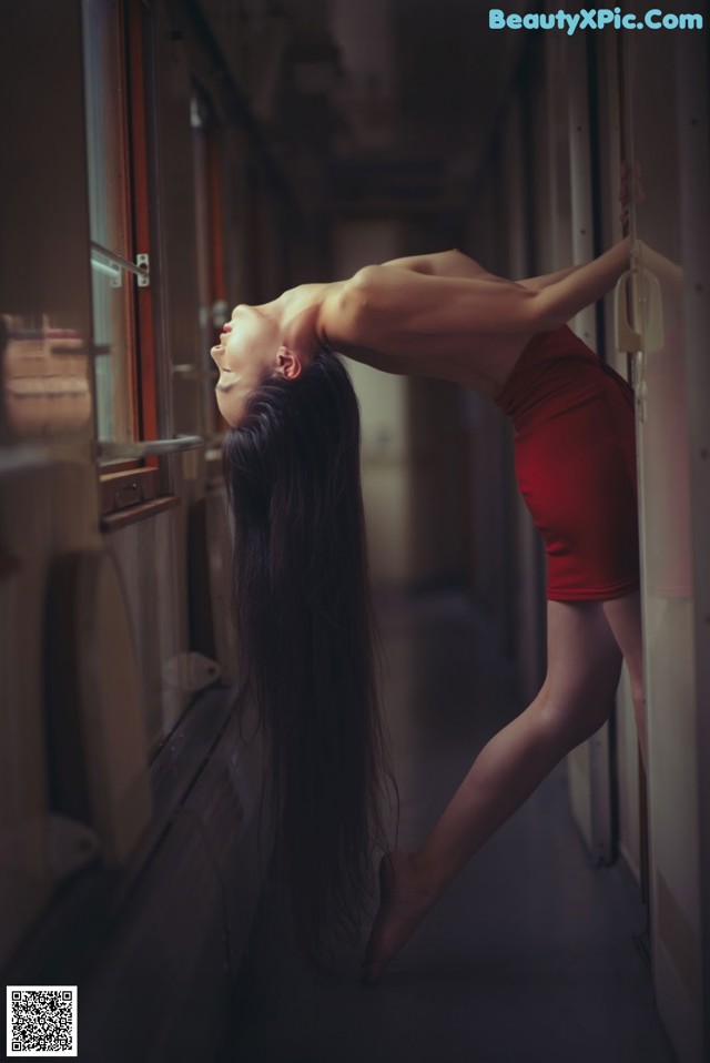 A woman in a red dress leaning against a window.