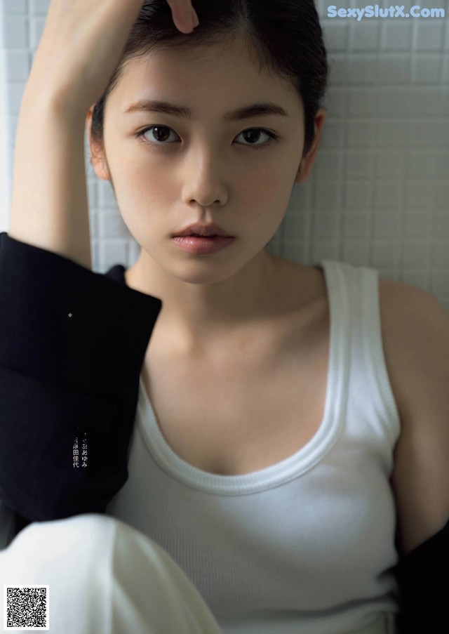 A woman in a white tank top sitting on a chair.