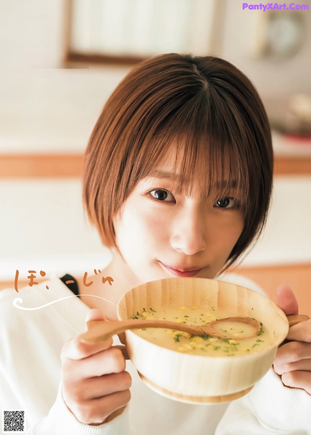 A woman holding a bowl of soup with a wooden spoon.