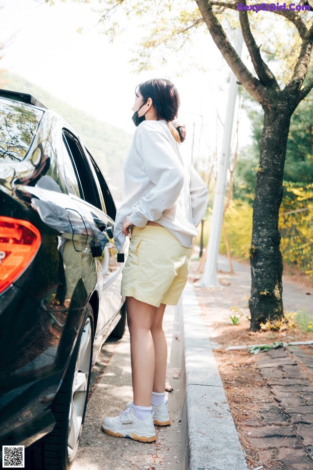 A woman wearing a face mask standing next to a car.