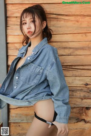 A woman in a denim jacket leaning against a wooden wall.