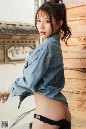 A woman in a denim jacket leaning against a wooden wall.