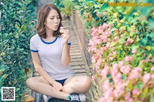 A woman sitting on a wooden bench in front of flowers.