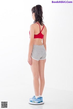 A young woman in a red top and gray shorts sitting on the floor.