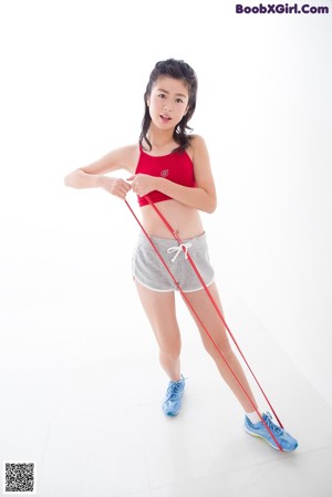 A woman in a red top and gray shorts leaning against a wall.