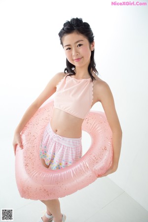 A young woman leaning against a wall in a pink bikini top and skirt.