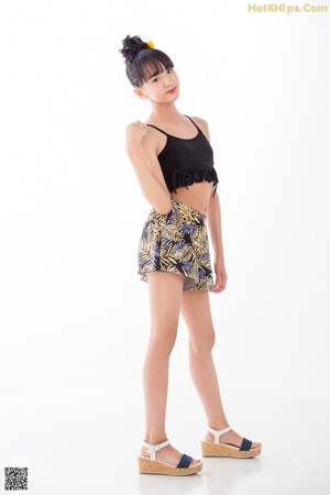A woman in a black top and yellow shorts with a sunflower in her hair.