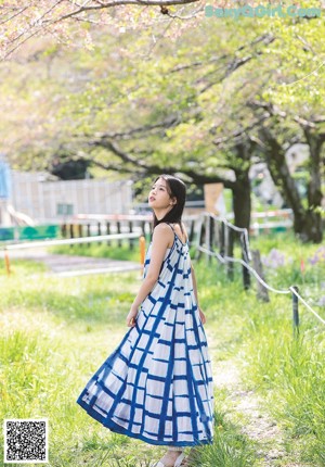 A woman in a white top and blue skirt holding a book.