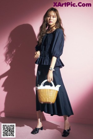 A woman standing in front of a pink wall holding a white bag.
