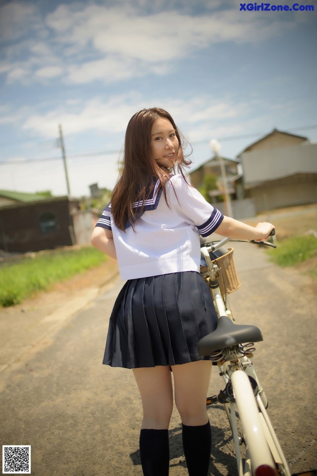 A woman in a school uniform standing next to a bike.