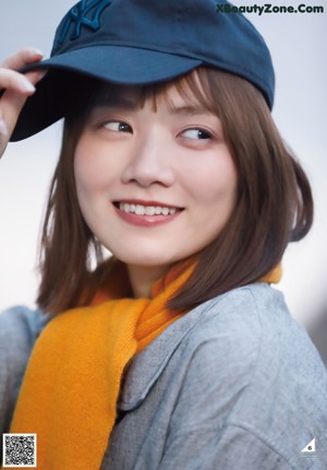 A young woman in a blue sweater leaning against a wall.