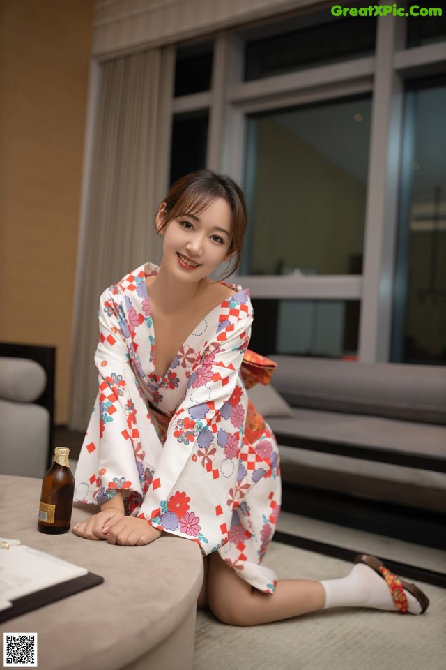 A woman in a kimono sitting on a couch next to a bottle of beer.