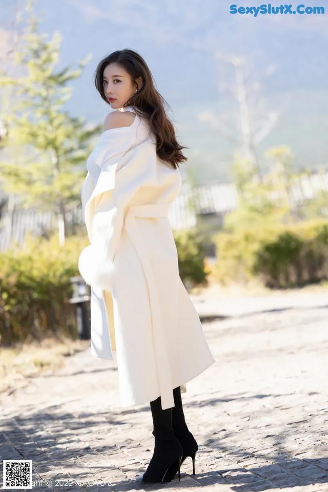 A woman in a white coat is standing on a cobblestone road.