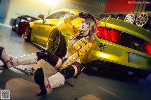 A woman in a yellow jacket and hat posing in front of a red car.