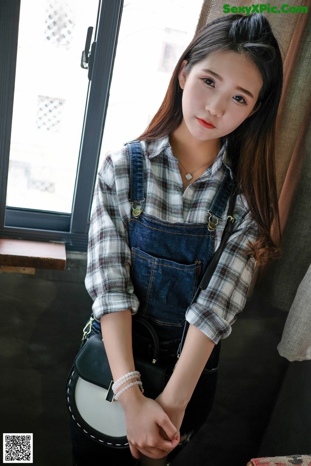 A young woman wearing overalls and a plaid shirt.