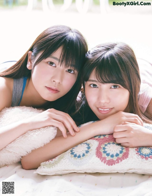 A couple of young women laying on top of a bed.