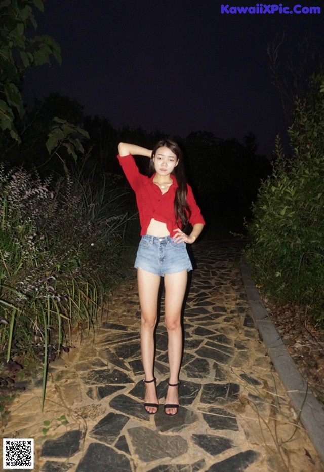 A woman in a red shirt and denim shorts posing for a picture.