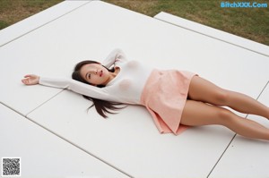 A naked woman sitting on top of a bed next to a plant.