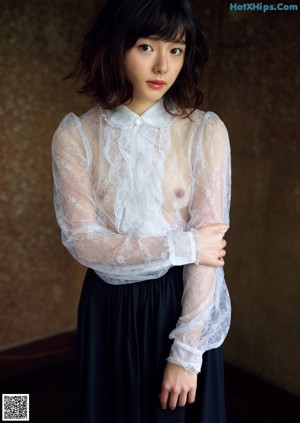 A woman in a white bodysuit leaning against a wooden pole.