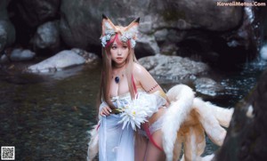 A woman in a white dress sitting on a rock next to a white wolf.