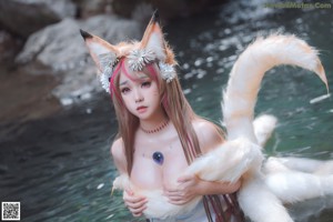 A woman in a white dress sitting on a rock next to a white wolf.