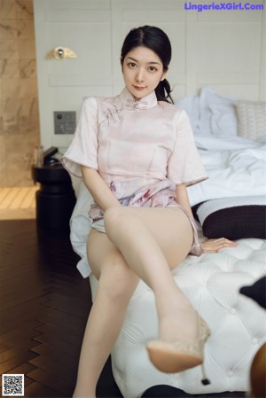 A woman in a pink dress sitting on a bed.